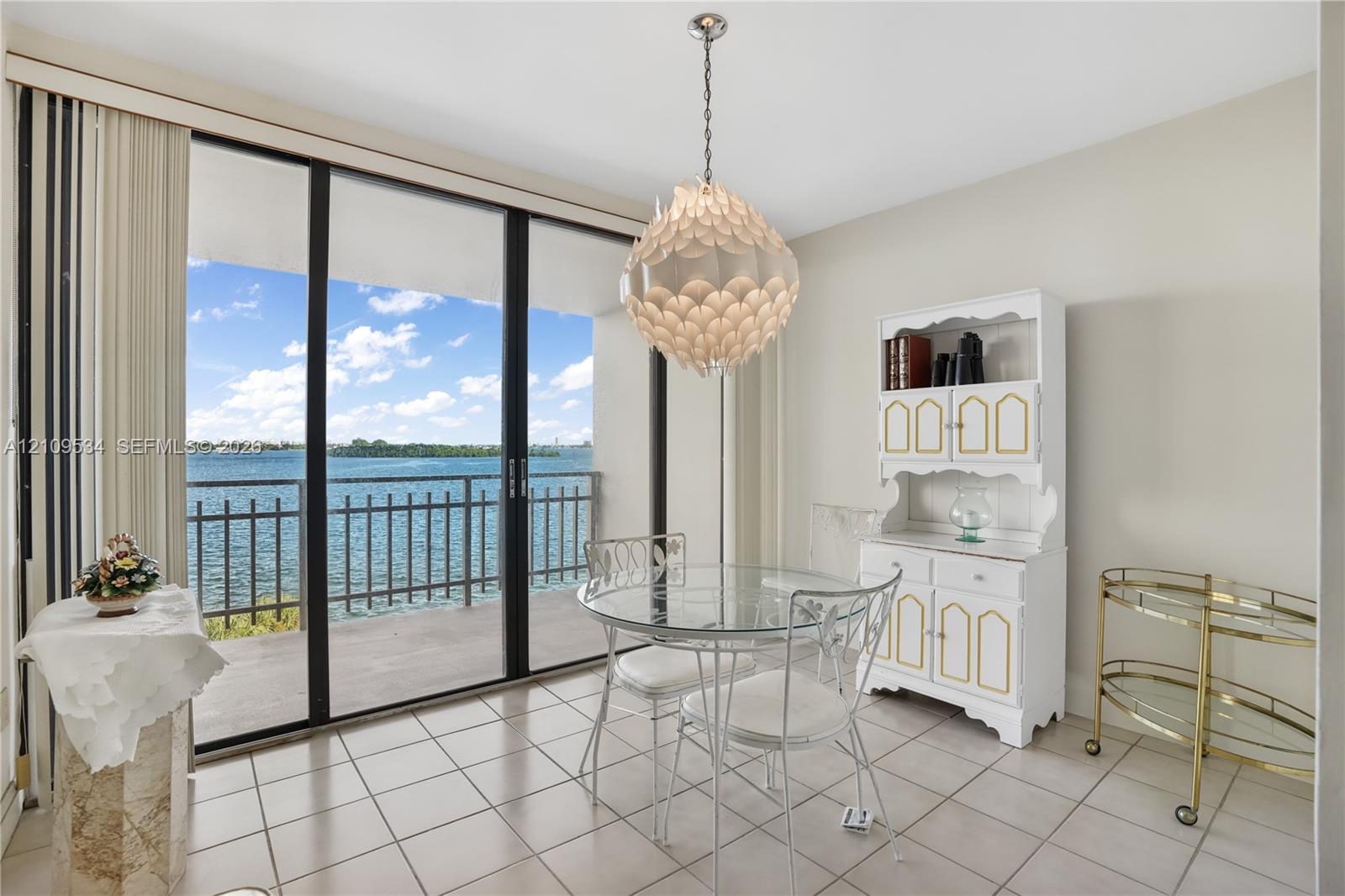 Floor-to-ceiling glass sliding doors opening to a covered balcony, ceramic tile flooring, and decorative tiered pendant lighting