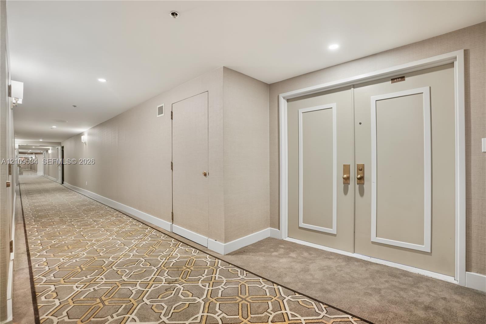 Hallway featuring recessed ceiling lighting, textured wall coverings, double doors with metallic hardware, and patterned carpeting