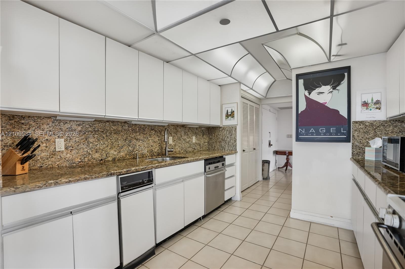 Kitchen featuring white flat-panel cabinetry, stone countertops, tiled flooring, integrated lighting, and stainless steel appliances