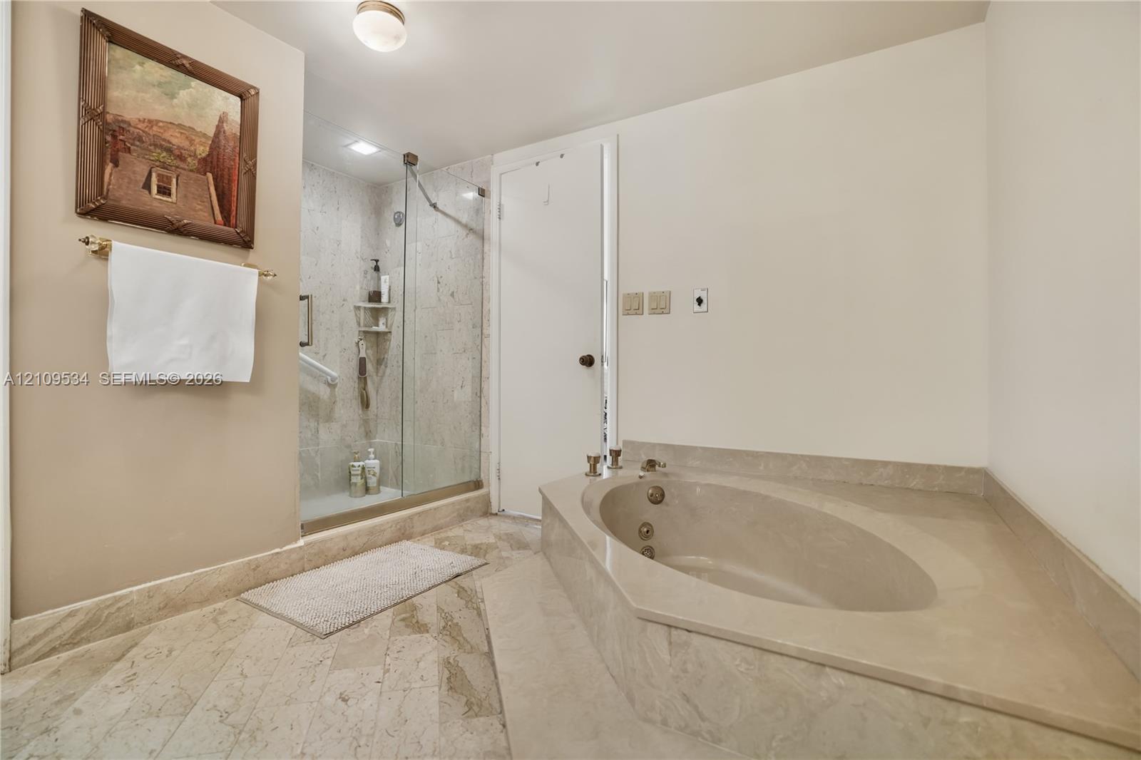 Jetted soaking tub with a stone-surround deck, walk-in shower enclosed by a frameless glass door, and stone tile flooring