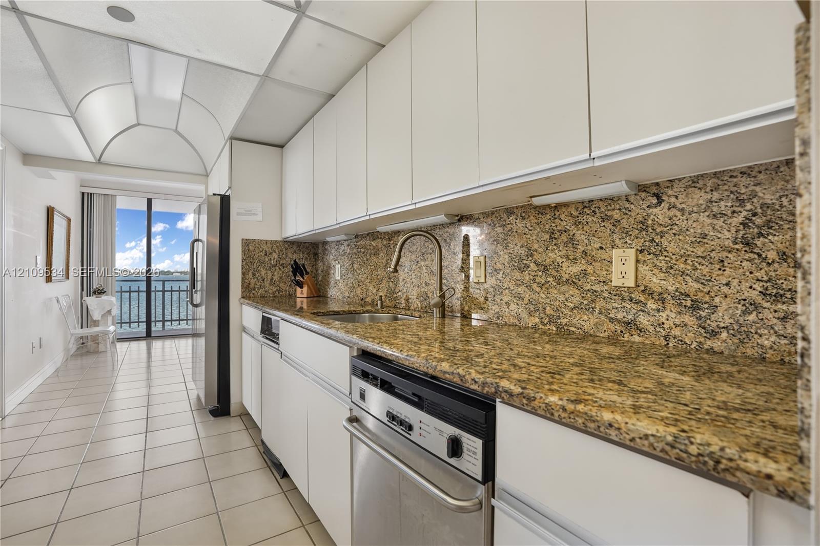 Kitchen featuring flat-panel white cabinetry, stone-finish countertops, stainless steel appliances, a high-arc faucet, and tile flooring