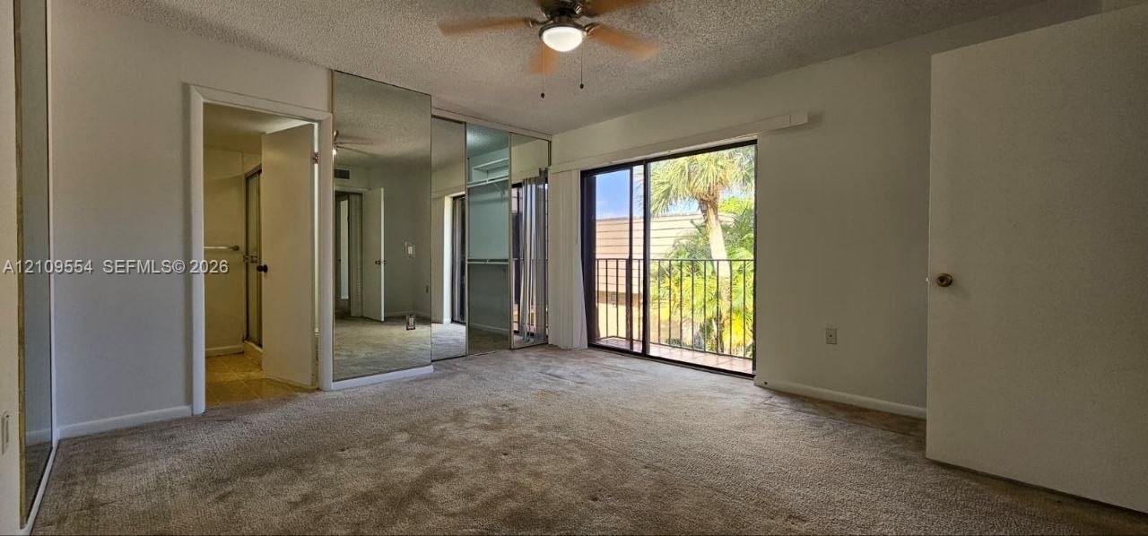 Sliding glass door opening to a private balcony, floor-to-ceiling mirrored closet doors, neutral wall-to-wall carpeting, and a ceiling-mounted light fixture