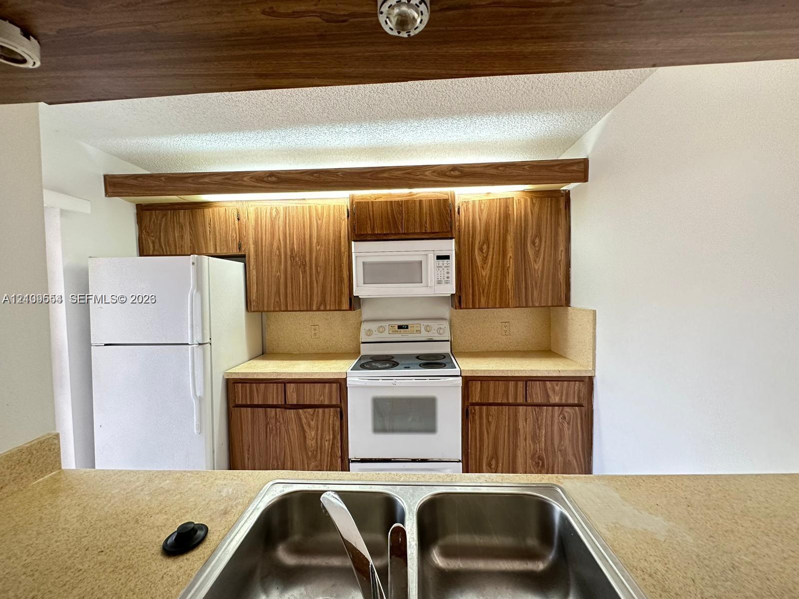 Kitchen featuring wood-finish cabinetry, a dual-basin stainless steel sink, solid-surface countertops, and a mounted microwave above the range