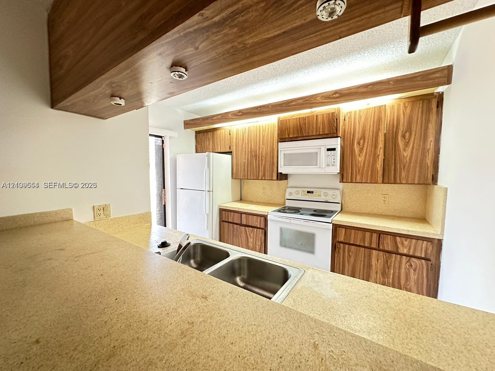 Kitchen featuring wood-grain cabinetry, solid surface countertops, a dual-basin stainless steel sink, and built-in appliances