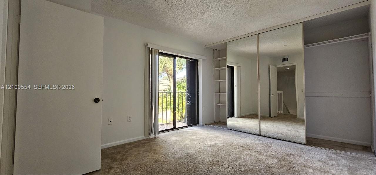 Interior space featuring carpeting, sliding glass doors to a balcony, mirrored closet doors, and built-in shelving