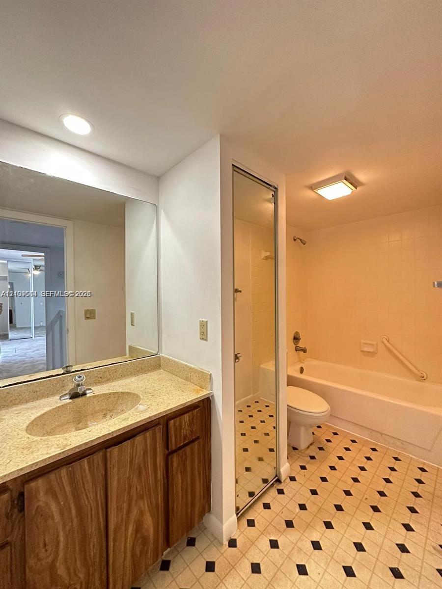 Bathroom featuring wood-finish cabinetry, stone-texture countertop with an integrated basin, wall-to-wall mirror, and geometric-patterned tile flooring