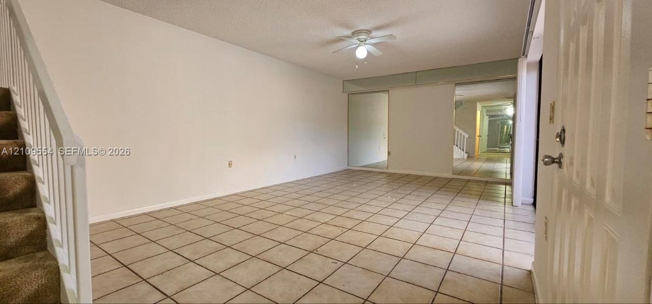Ceramic tile flooring, carpeted staircase with white railings, ceiling fan with integrated lighting, and wall-mounted mirror panels