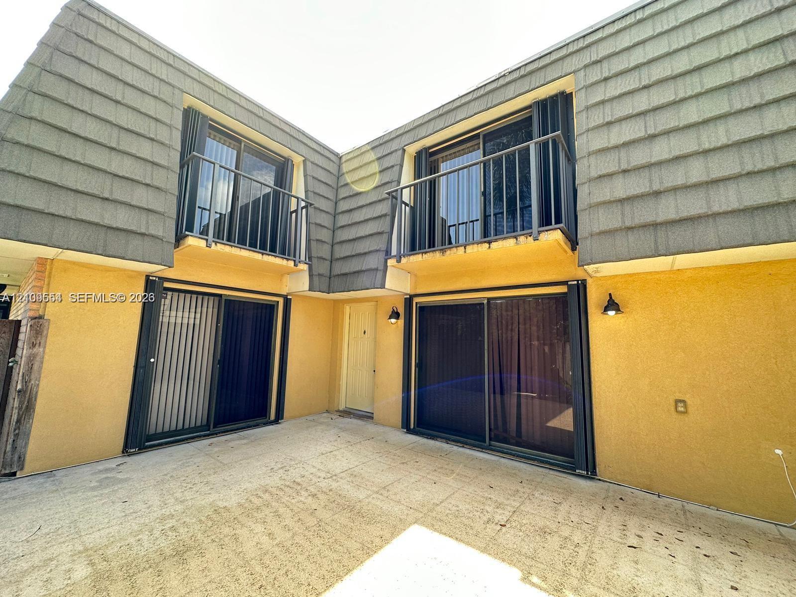 Exterior featuring two private balconies with metal railings, sliding glass doors on two levels, and a concrete patio area