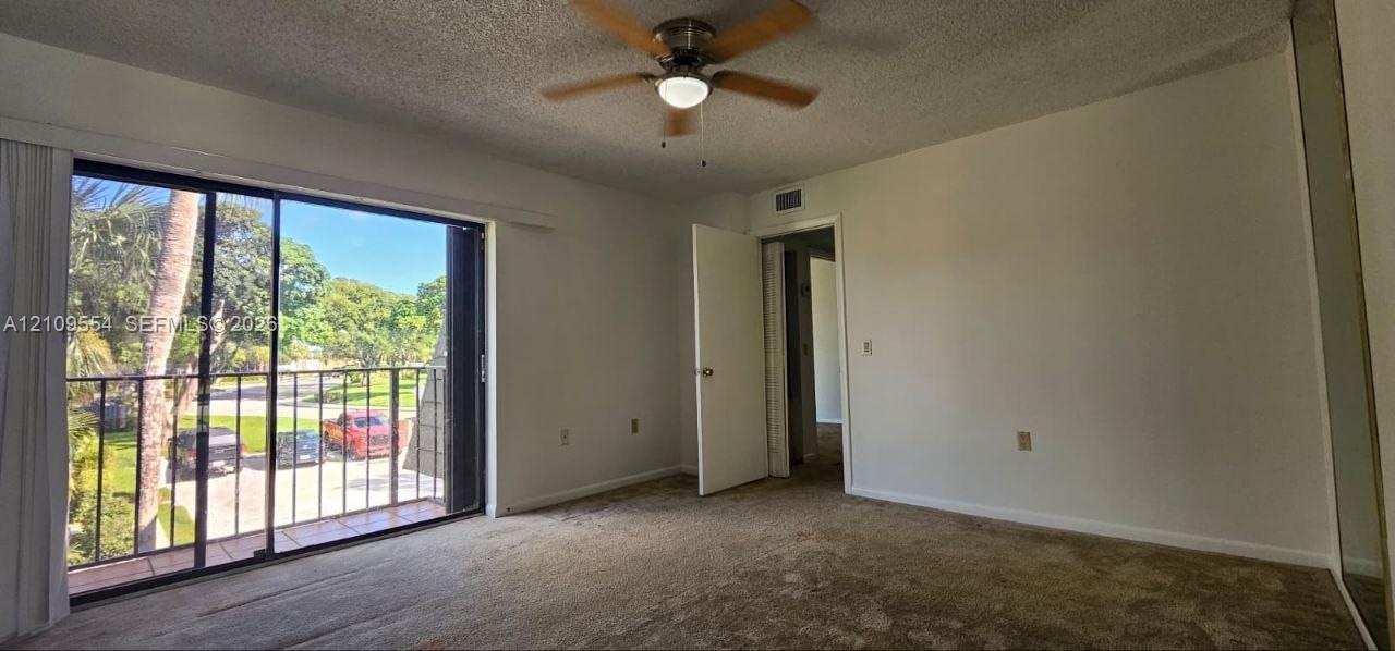 Interior space featuring floor-to-ceiling sliding glass doors, a private balcony with metal railing, wall-to-wall carpeting, and a ceiling-mounted light fixture with fan