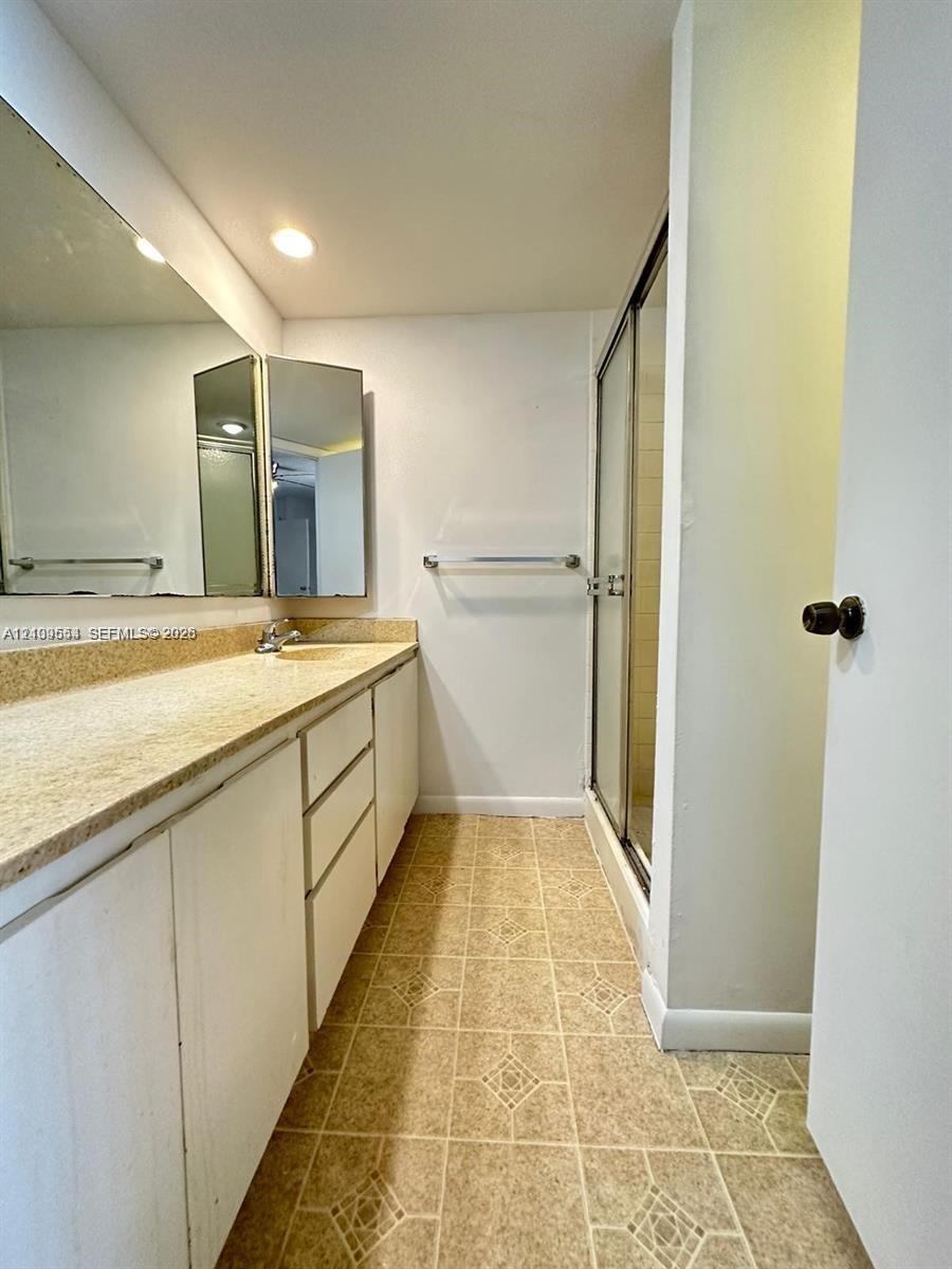 Bathroom featuring a full-width vanity with a neutral countertop, integrated sink, large wall-mounted mirror, and a walk-in shower with a glass enclosure