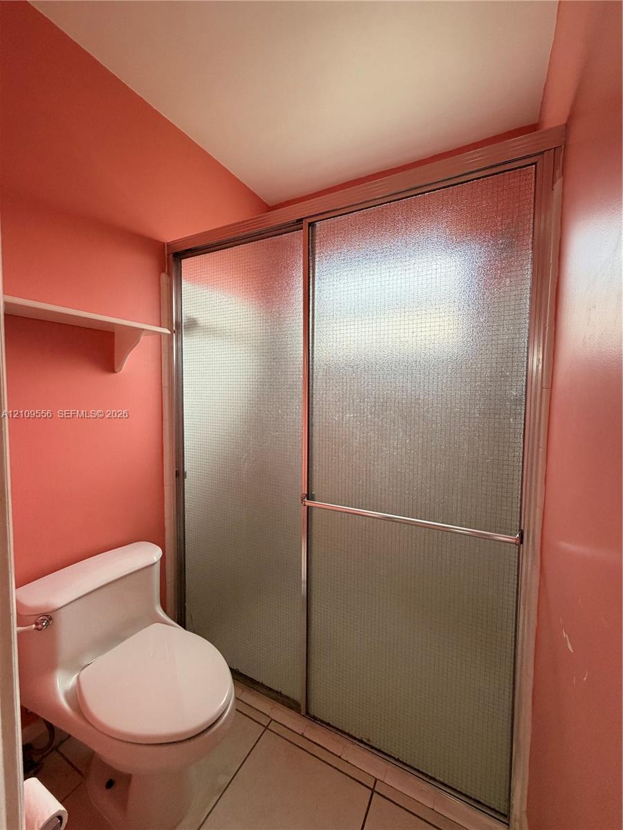 Shower enclosure with textured glass sliding doors and metal frame, white ceramic toilet, and tiled flooring