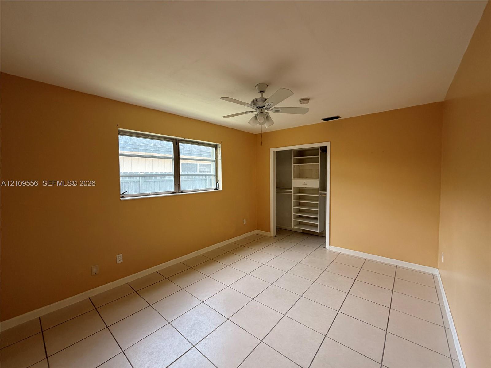 Room featuring tile flooring, multi-pane window, ceiling fan with integrated light fixture, and closet with built-in shelving