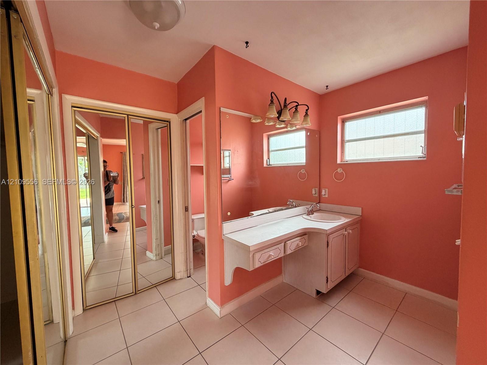 Vanity with integrated sink and storage cabinetry, large wall-mounted mirror, dual windows, and tile flooring