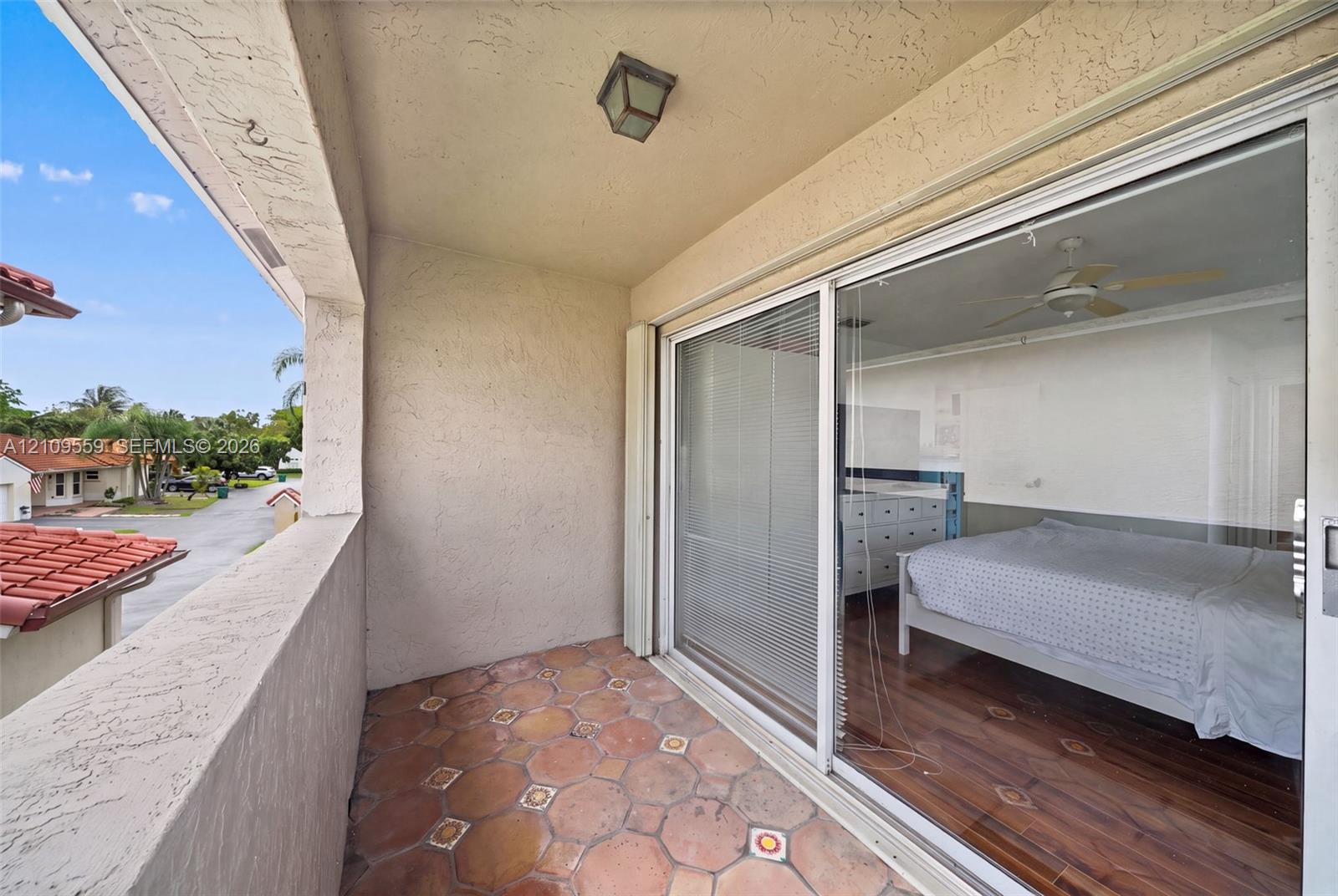 Covered balcony featuring patterned terra-cotta tile flooring, stucco walls, and sliding glass patio doors