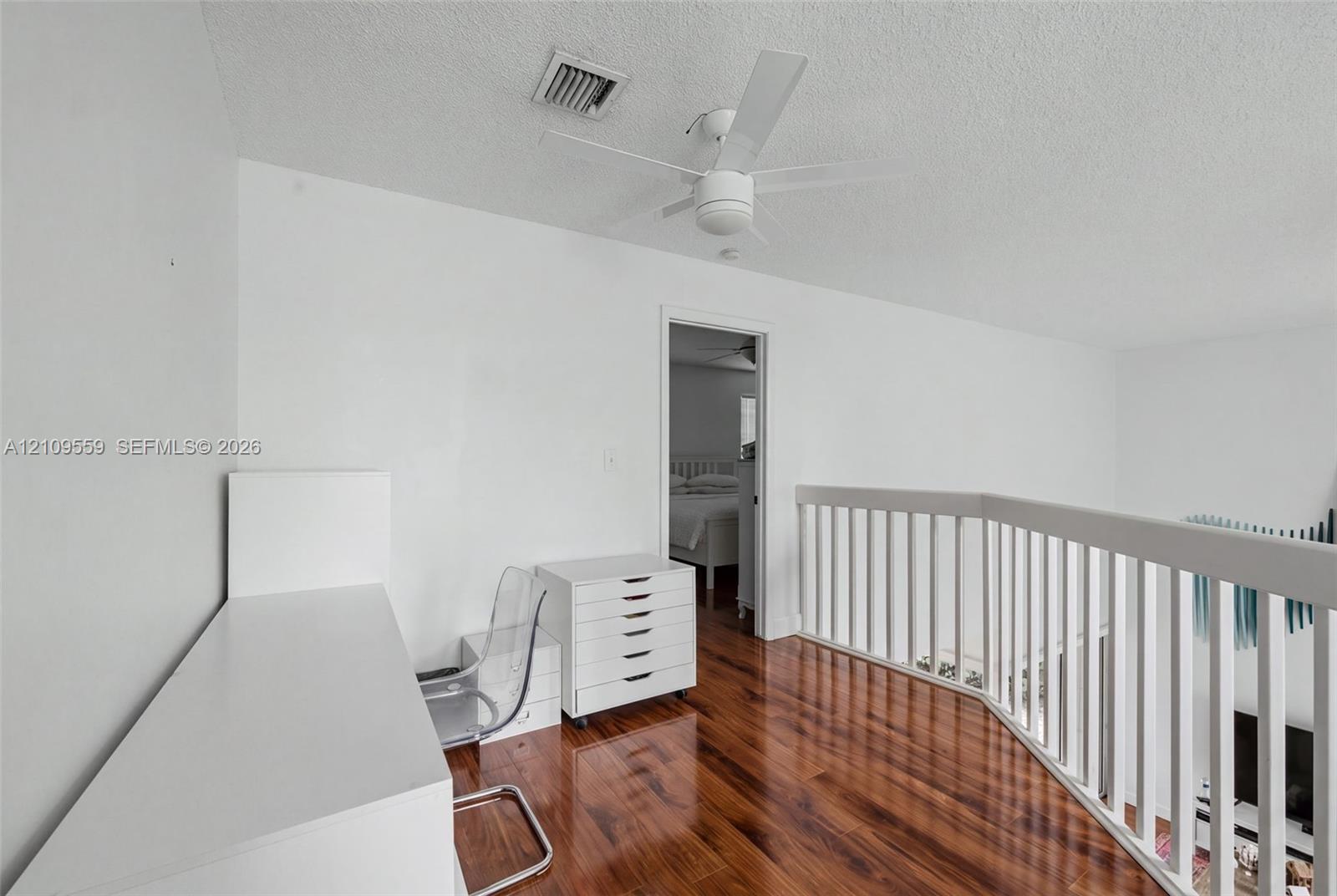 Wood-finish flooring, white spindle railing, and ceiling fan with integrated lighting