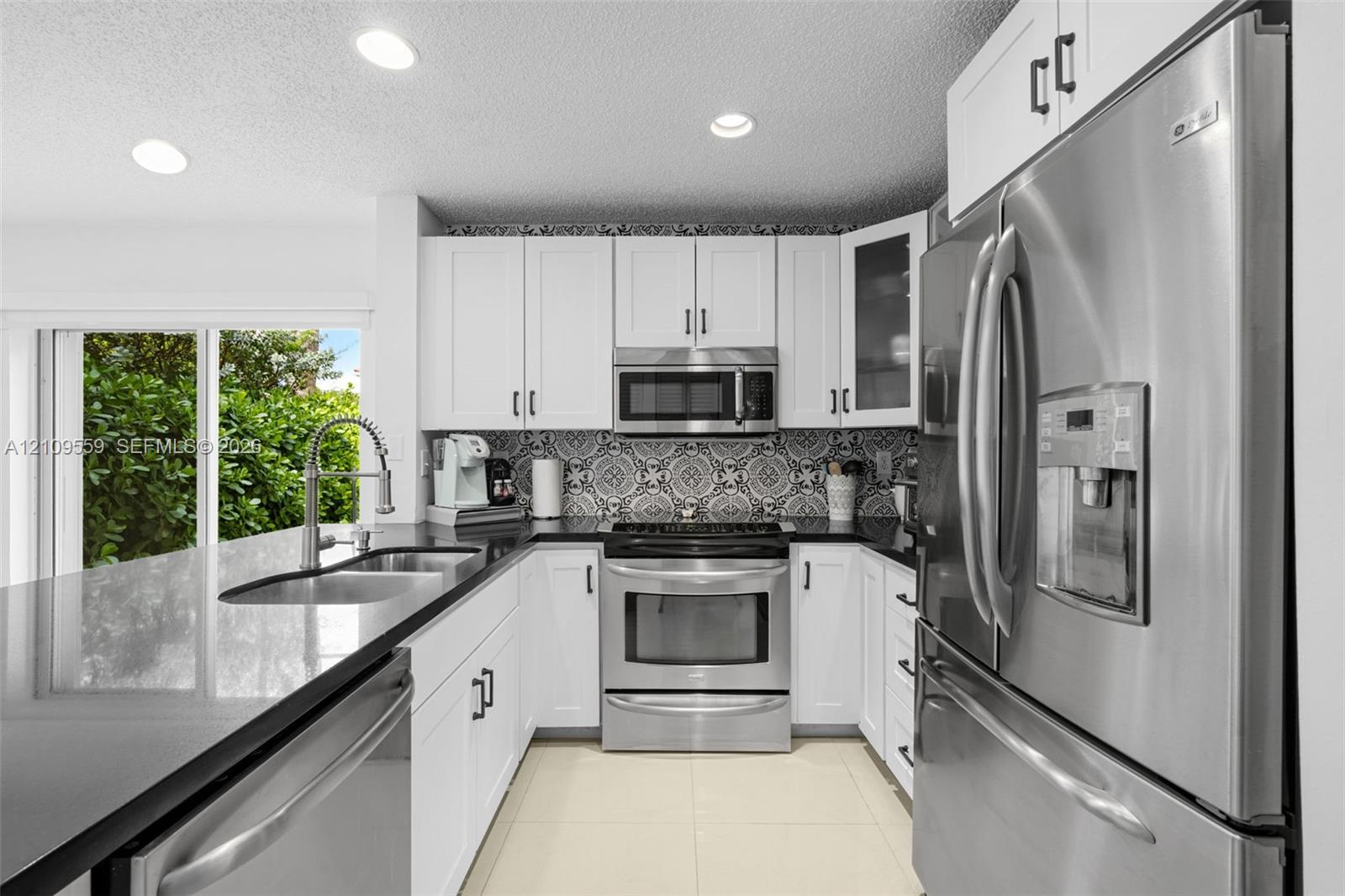 Kitchen featuring white shaker-style cabinetry, dark stone countertops, stainless steel appliances, patterned tile backsplash, and recessed lighting