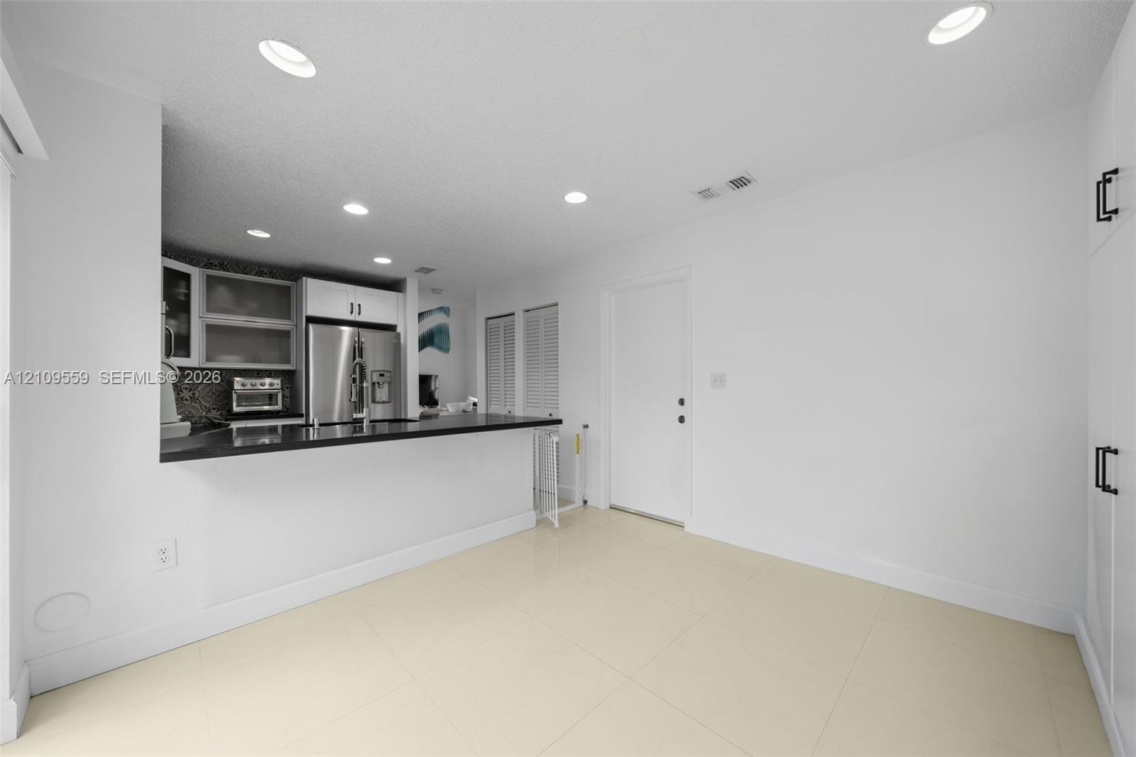 Kitchen featuring a breakfast bar with dark countertop, stainless steel refrigerator, recessed lighting, tile flooring, and floor-to-ceiling built-in cabinetry