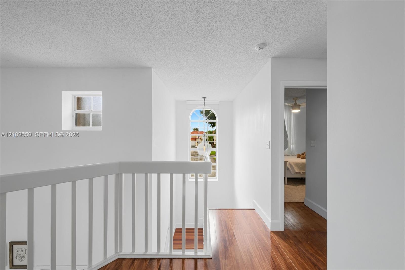 Arched window with decorative grille, white spindle railing, wood-finish flooring, and recessed ceiling-mounted lighting
