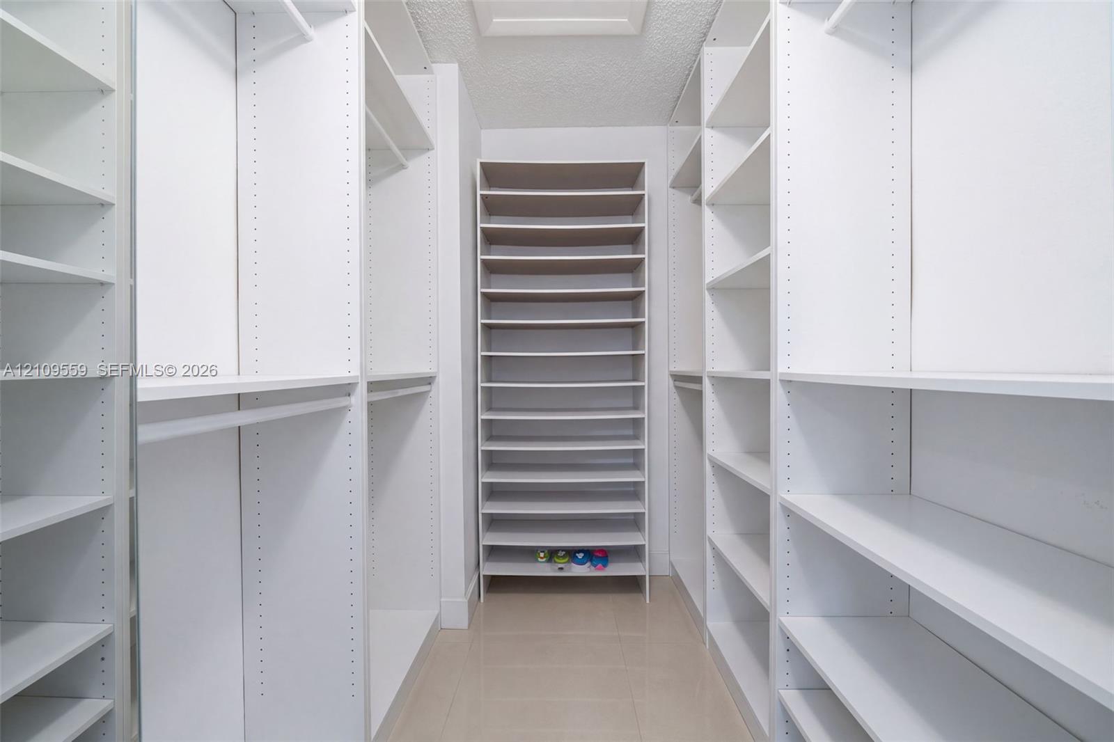 Walk-in closet featuring extensive built-in white shelving, multiple hanging rods, and dedicated floor-to-ceiling shoe storage
