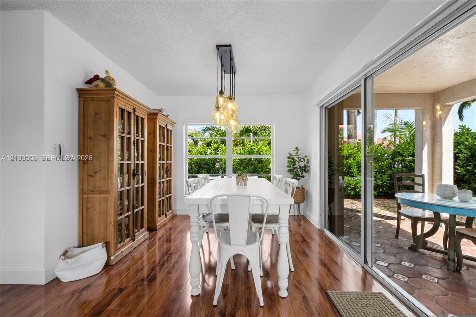 Wood-finish flooring, built-in floor-to-ceiling cabinetry, multi-pendant light fixture, and floor-to-ceiling sliding glass doors opening to a covered patio with terracotta-style tile flooring