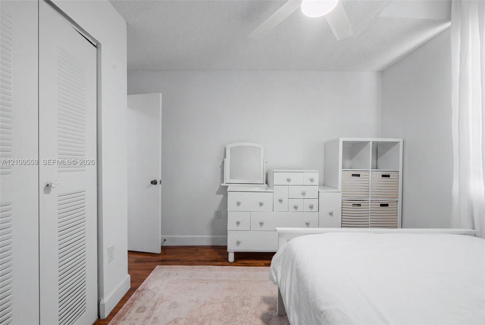 Neutral interior featuring wood-finish flooring, white louvered closet doors, and a ceiling-mounted fan with light fixture