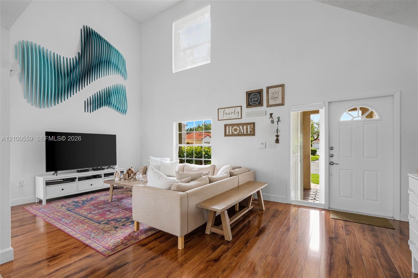 Vaulted ceilings, wood-finish flooring, high-reaching windows, and a panelled front door with an arched glass insert