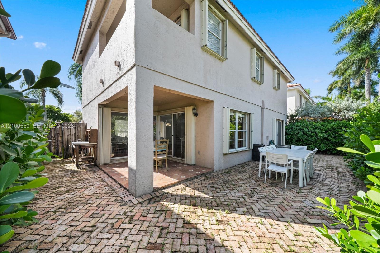 Two-story exterior featuring a covered patio, brick-paver hardscaping, upper-level balcony, and exterior light fixtures
