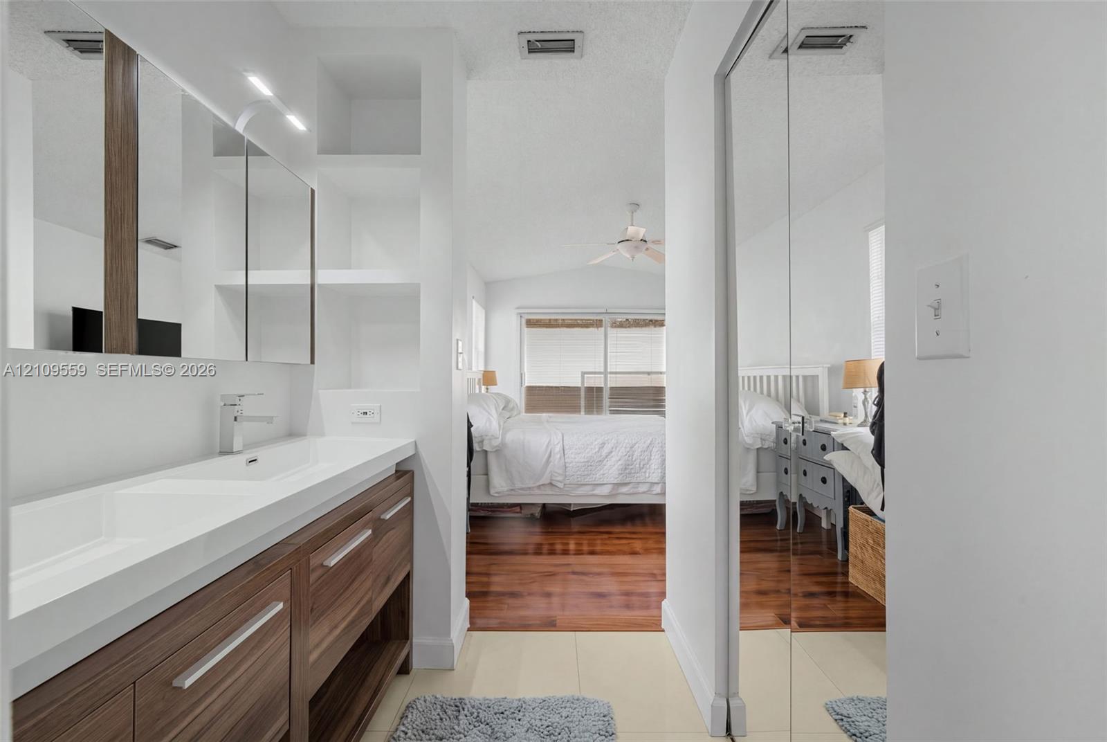 Vanity featuring a dual-sink integrated basin, wood-finish cabinetry, built-in shelving, and floor-to-ceiling mirrored closet doors