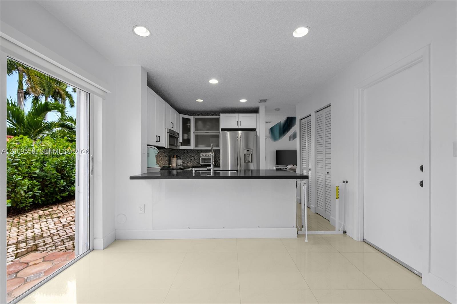 Kitchen featuring white shaker-style cabinetry, dark stone countertops, stainless steel appliances, tile flooring, and sliding glass doors