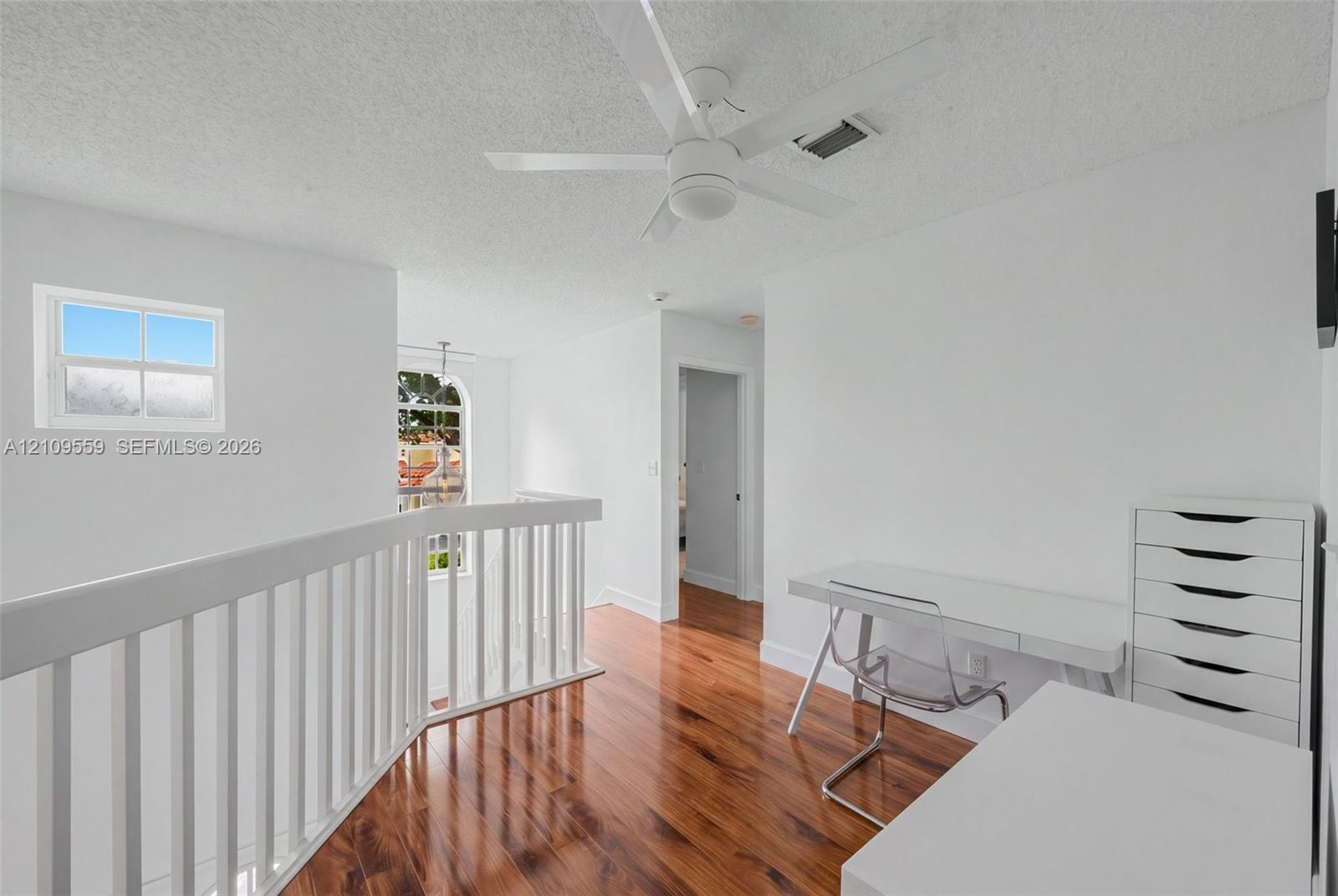 Wood-finish flooring, white wooden balustrade, arched multi-pane window, and white ceiling fan