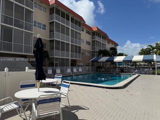 Community swimming pool featuring a paved deck, permanent blue-and-white striped shade structure, and multi-story building exterior with screened balconies