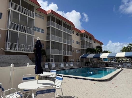 Multi-story building featuring screened-in balconies, a swimming pool with paved deck, and a striped overhead canopy
