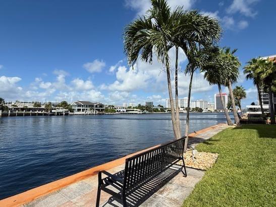Waterfront setting featuring a concrete seawall, manicured lawn, and mature palm trees