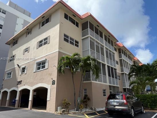 Multi-story building featuring stucco exterior, new roof, covered parking level with arched openings, and screened balconies