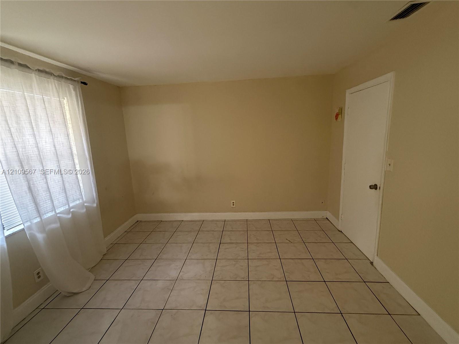 Interior room featuring neutral wall paint, large-format tile flooring, a window with fixed hardware, and a single-panel interior door Interior room featuring neutral wall paint, large-format tile flooring, a window with fixed hardware, and a single-panel interior door