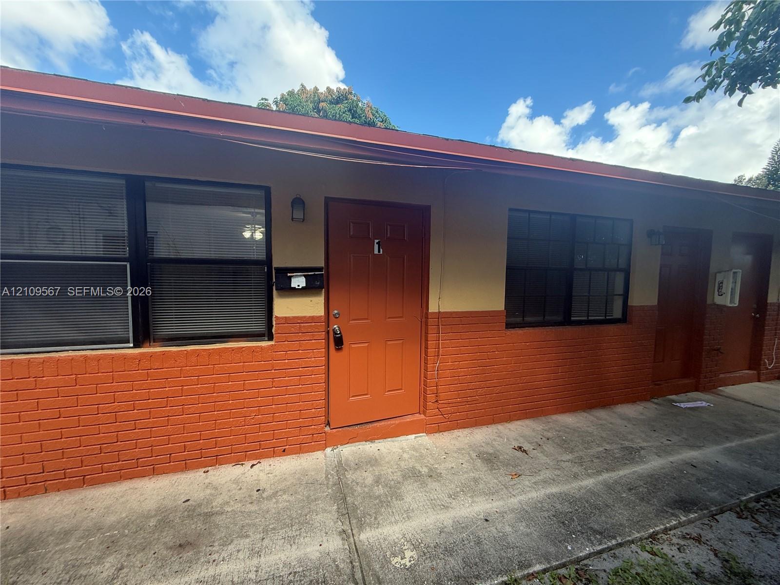 Exterior featuring a two-tone painted facade, lower-level brick masonry, multi-pane windows, and a concrete walkway Exterior featuring a two-tone painted facade, lower-level brick masonry, multi-pane windows, and a concrete walkway