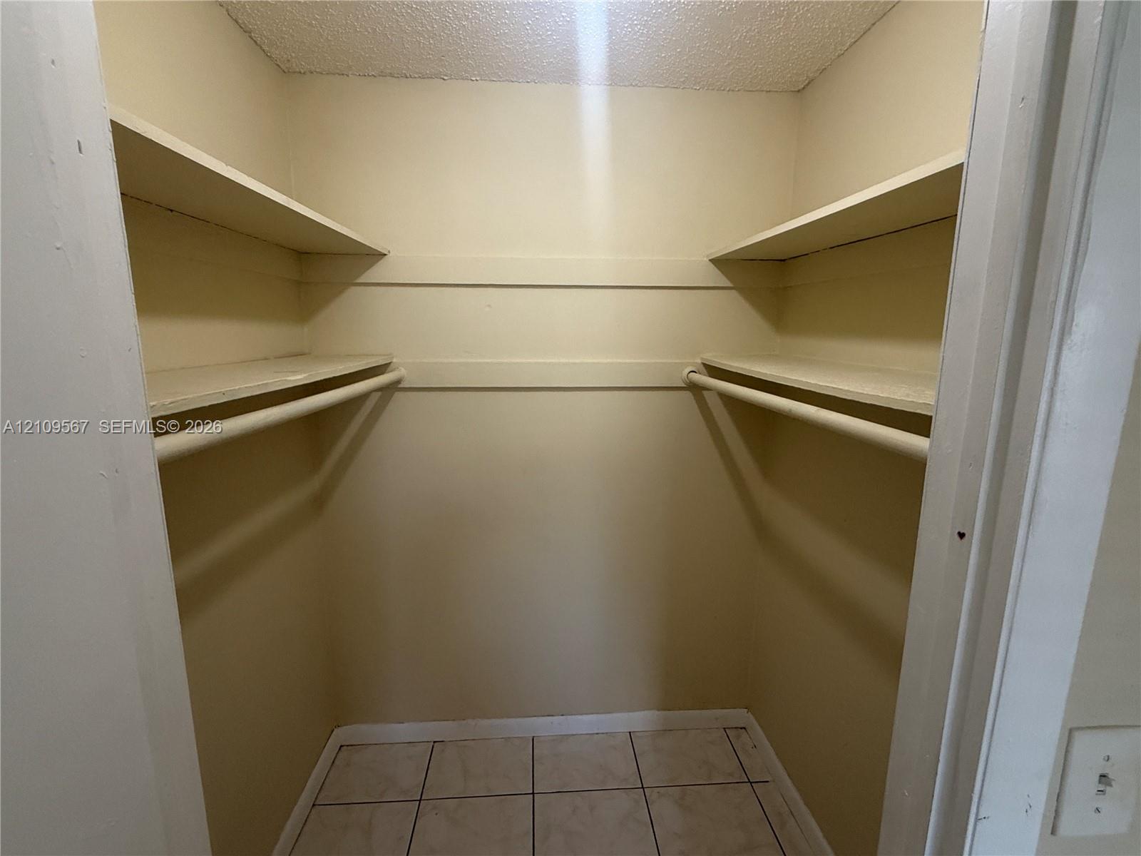 Walk-in storage space featuring ceramic tile flooring, built-in shelving, and dual hanging rods