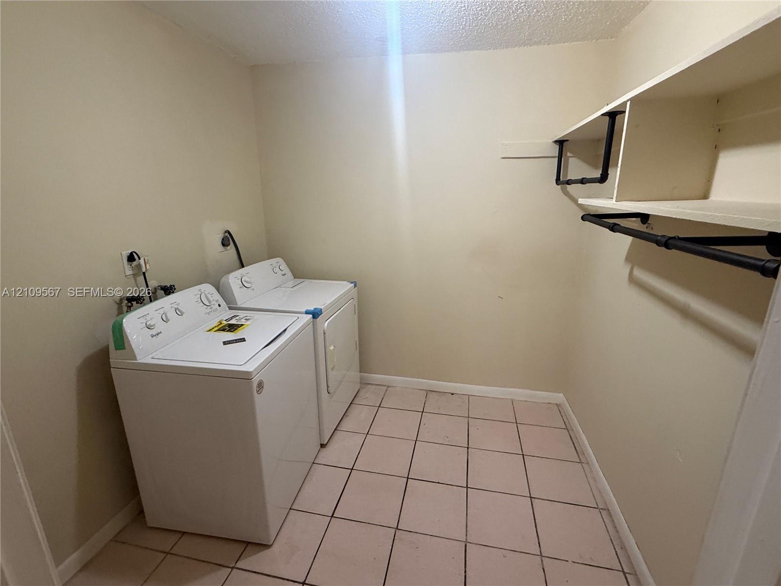 Laundry area featuring white appliances, tile flooring, and built-in shelving with an industrial-style pipe clothing rack Laundry area featuring white appliances, tile flooring, and built-in shelving with an industrial-style pipe clothing rack