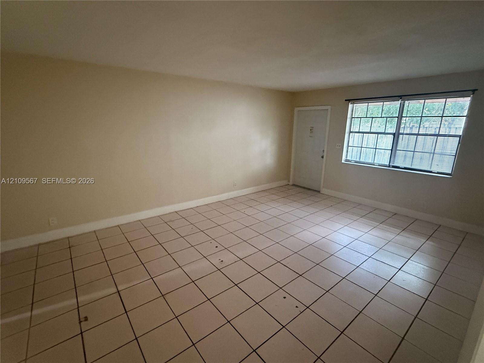 Neutral-toned interior space featuring light-colored tile flooring, smooth walls, and a window with a colonial grille pattern Neutral-toned interior space featuring light-colored tile flooring, smooth walls, and a window with a colonial grille pattern