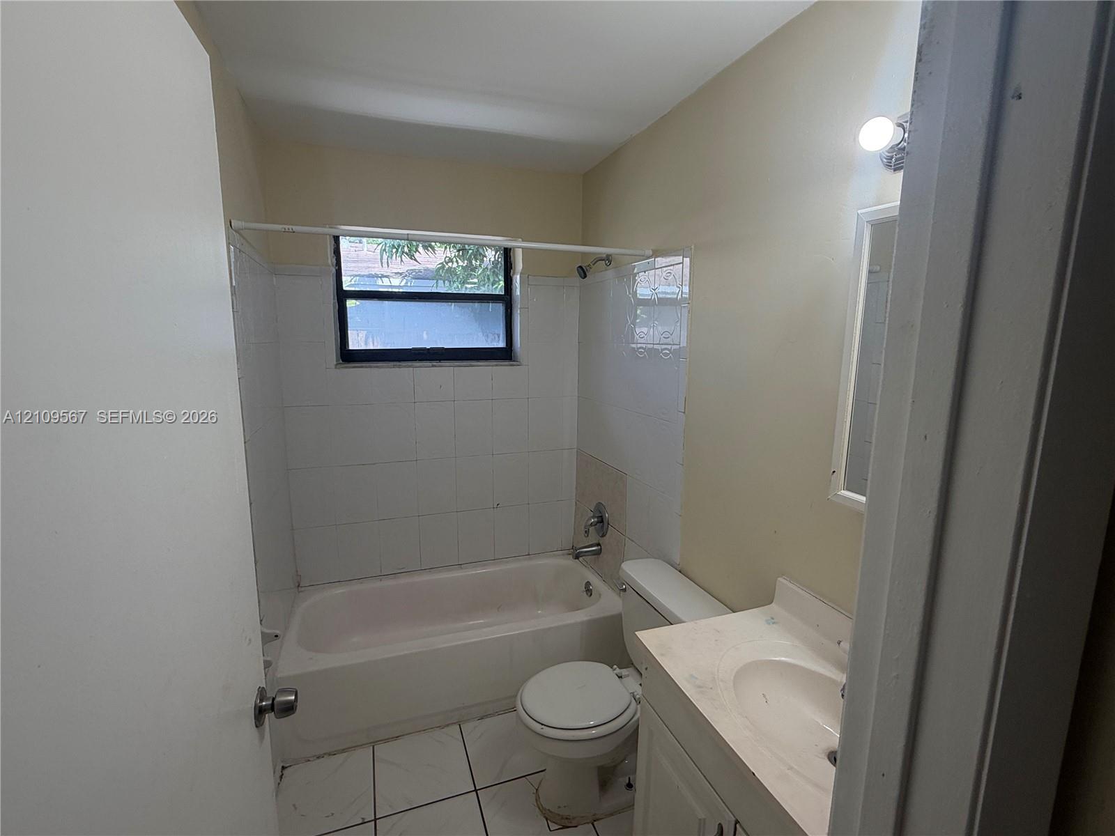 Bathroom featuring a white vanity with integrated sink, porcelain tile flooring, white wall-surround tub, and wall-mounted light fixture
