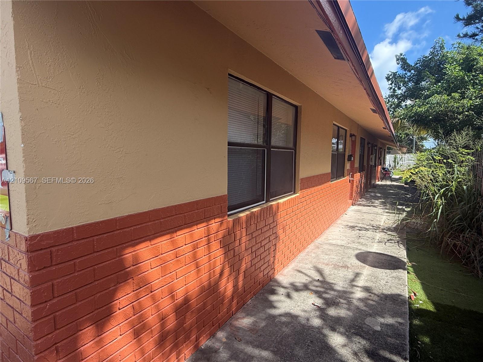 Exterior facade featuring a combination of textured stucco and brick masonry, concrete walkway, and window groupings with dark frames Exterior facade featuring a combination of textured stucco and brick masonry, concrete walkway, and window groupings with dark frames