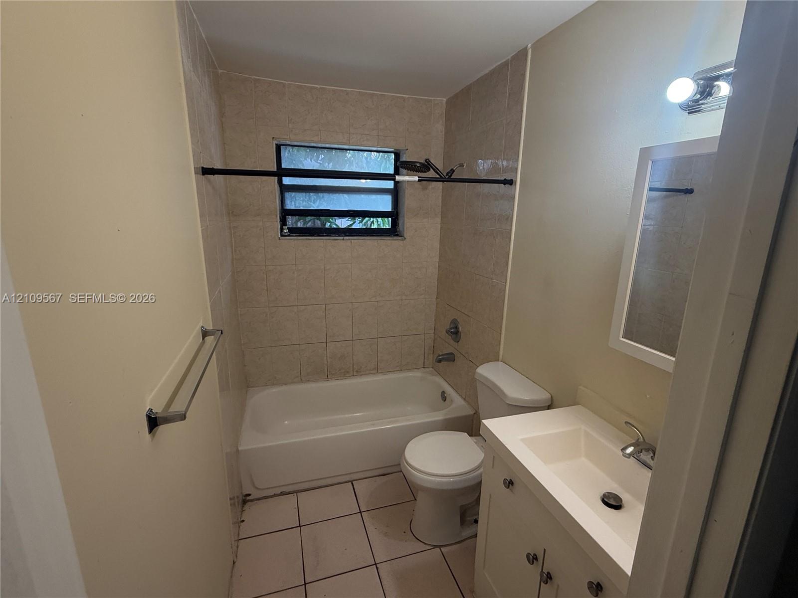 Full bathroom featuring a tub-shower combination with tiled surround, light-colored vanity with integrated sink, rectangular tile flooring, and wall-mounted vanity lighting Full bathroom featuring a tub-shower combination with tiled surround, light-colored vanity with integrated sink, rectangular tile flooring, and wall-mounted vanity lighting