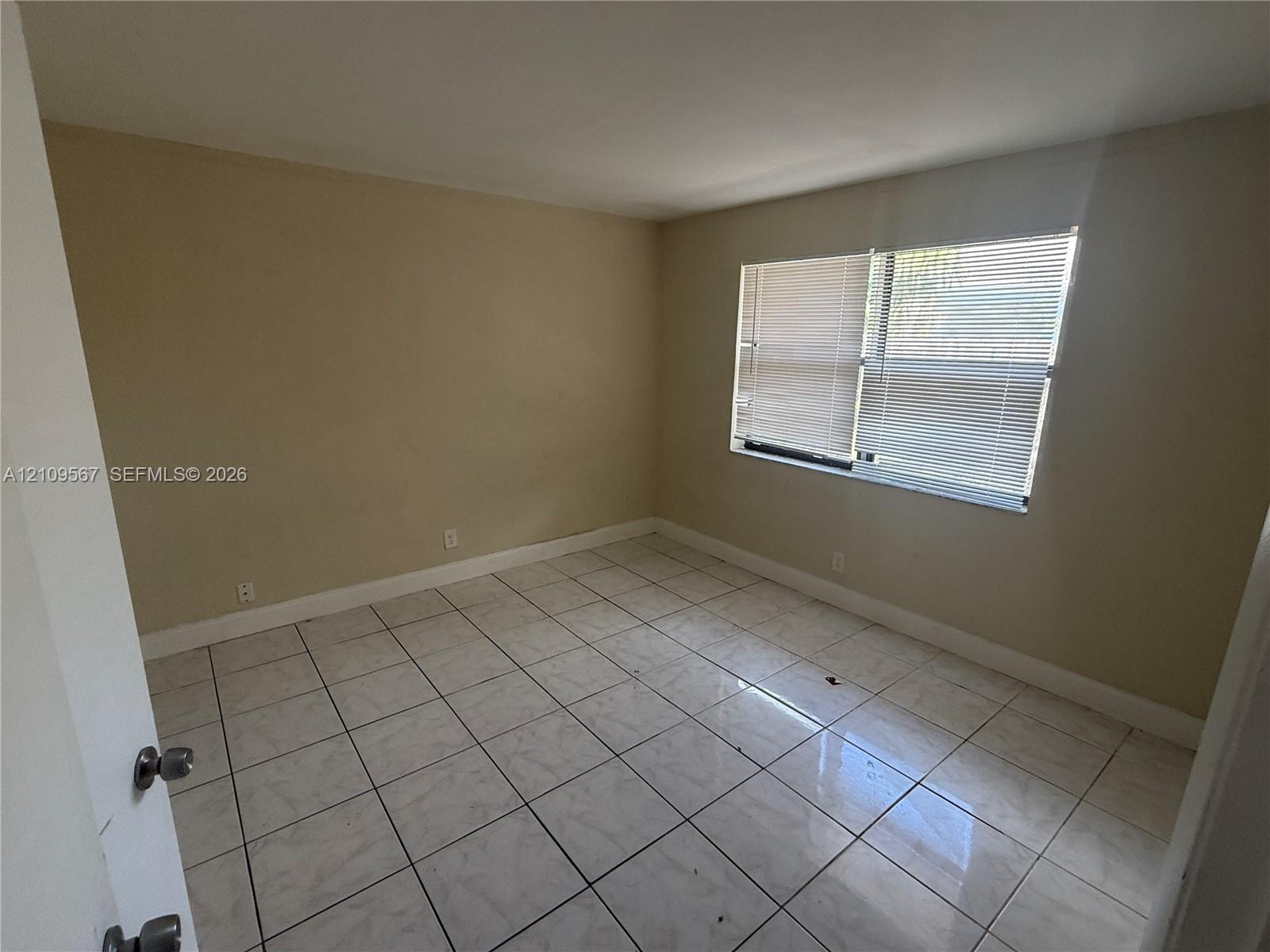 Room featuring large-format ceramic tile flooring and multi-pane window with horizontal blinds