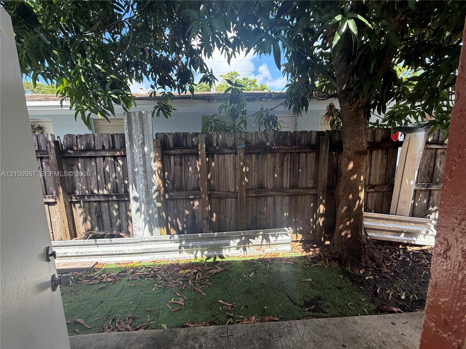 Outdoor area featuring a concrete patio, synthetic turf lawn, mature tree, and wood-panel privacy fencing