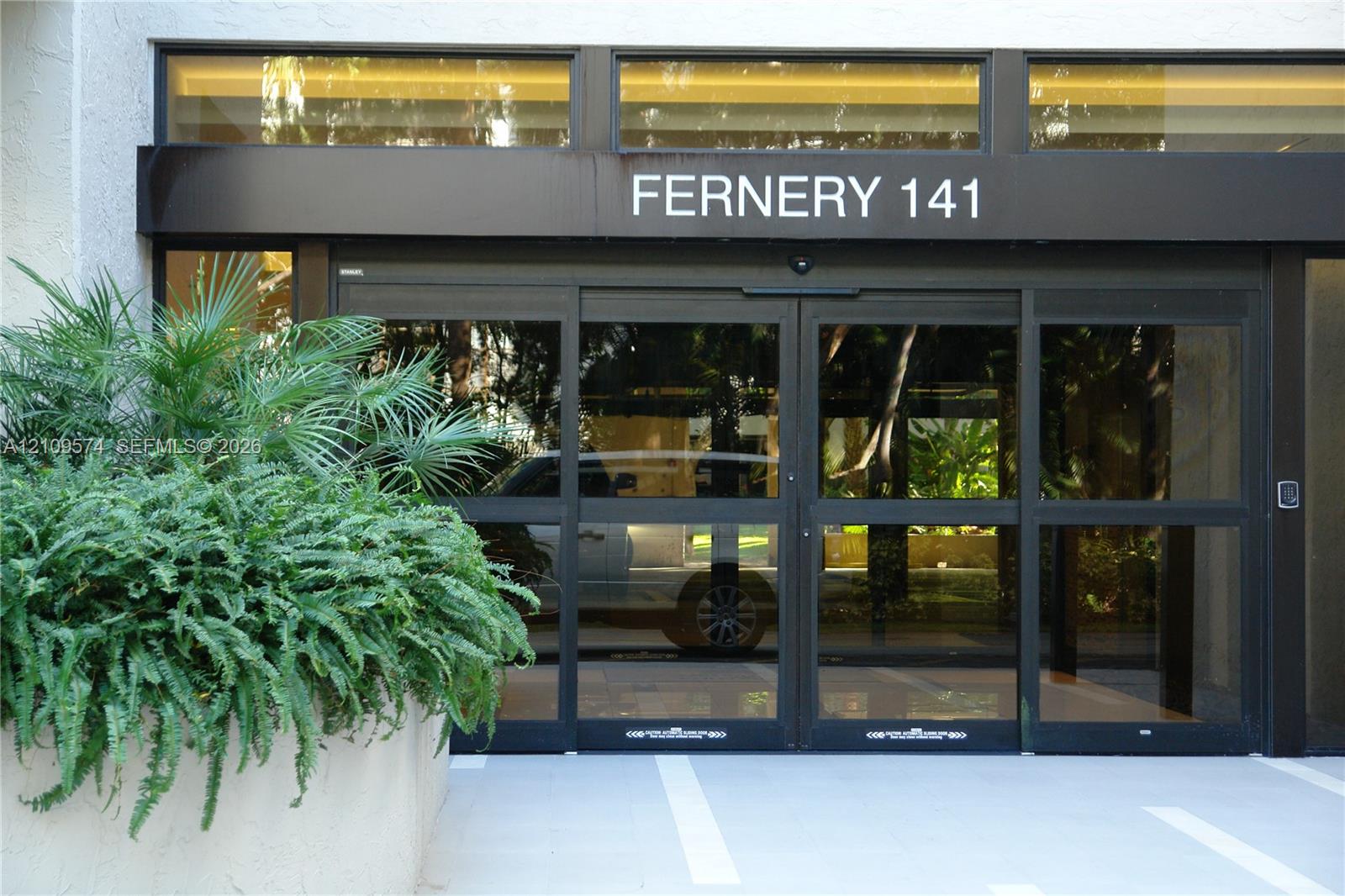 Entrance featuring automated sliding glass doors, black metal framing, transom windows, and a concrete planter