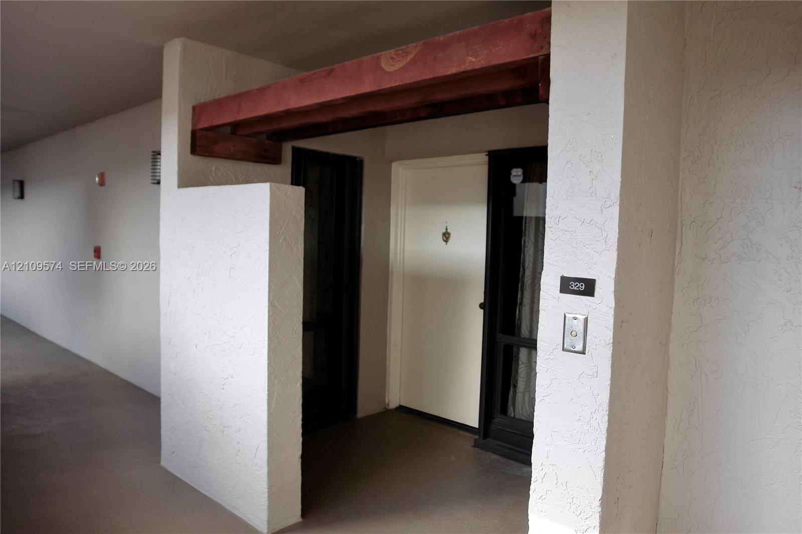 Covered entryway featuring a textured stucco facade, exposed wood beam accent, and a solid-core front door Covered entryway featuring a textured stucco facade, exposed wood beam accent, and a solid-core front door