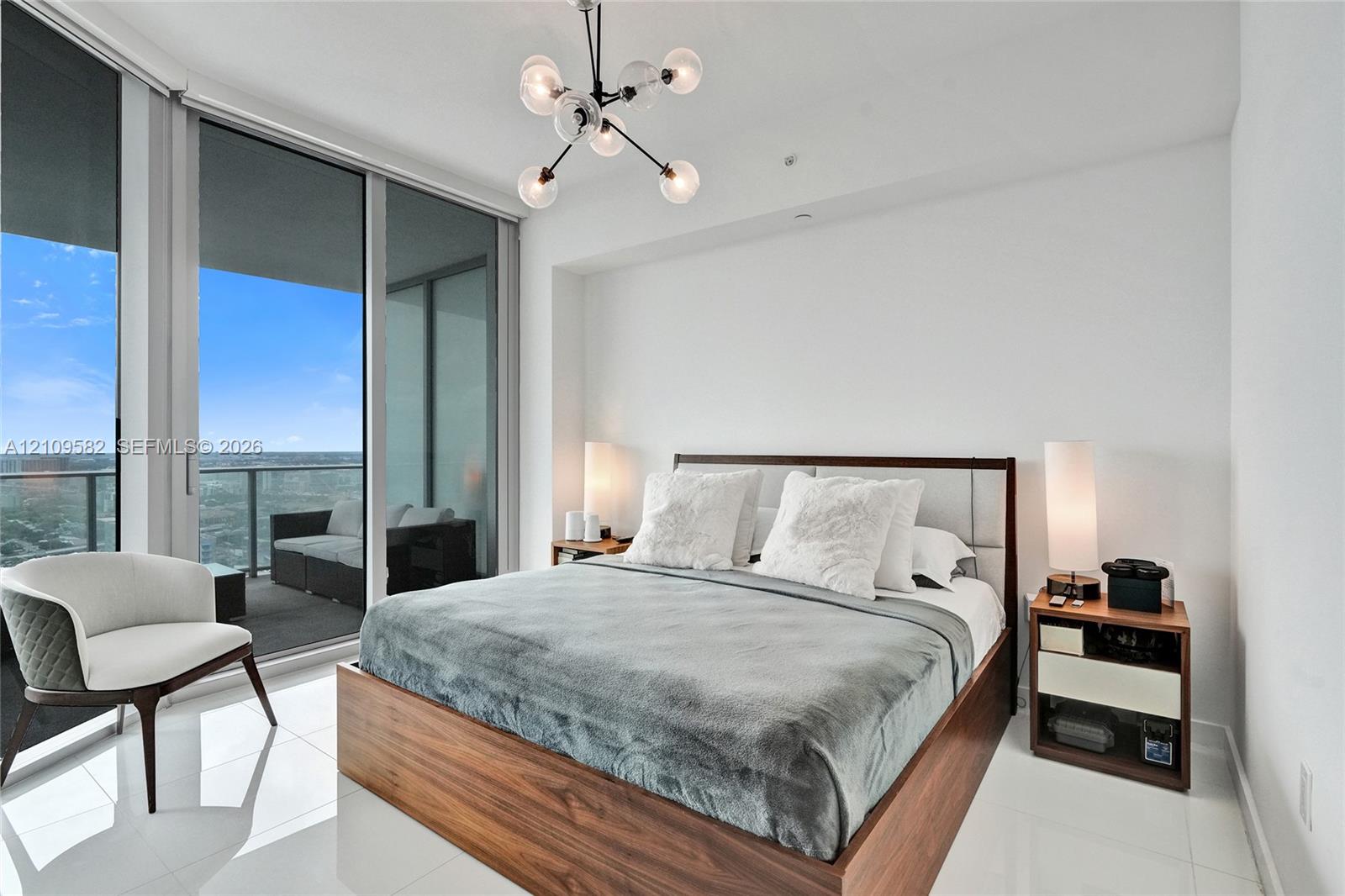 Floor-to-ceiling glass sliding doors, private balcony with metal railing, polished tile flooring, and multi-arm geometric ceiling light fixture
