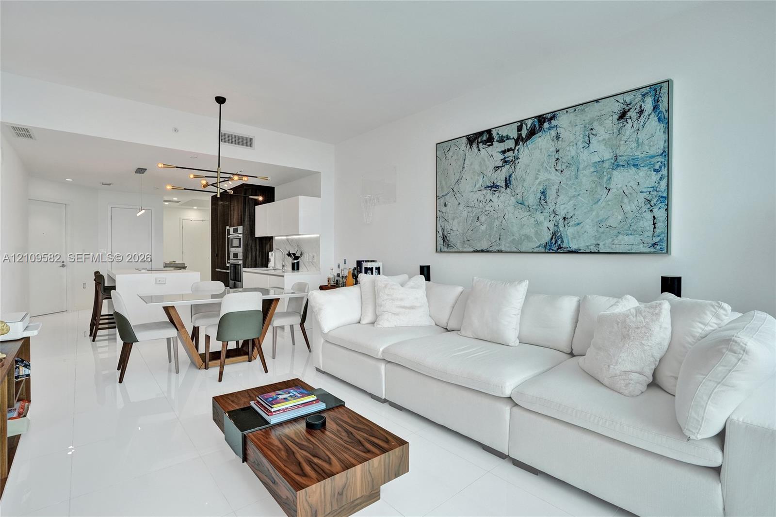Open-concept area featuring polished white tile flooring, modern multi-arm sputnik chandelier, and high-gloss cabinetry