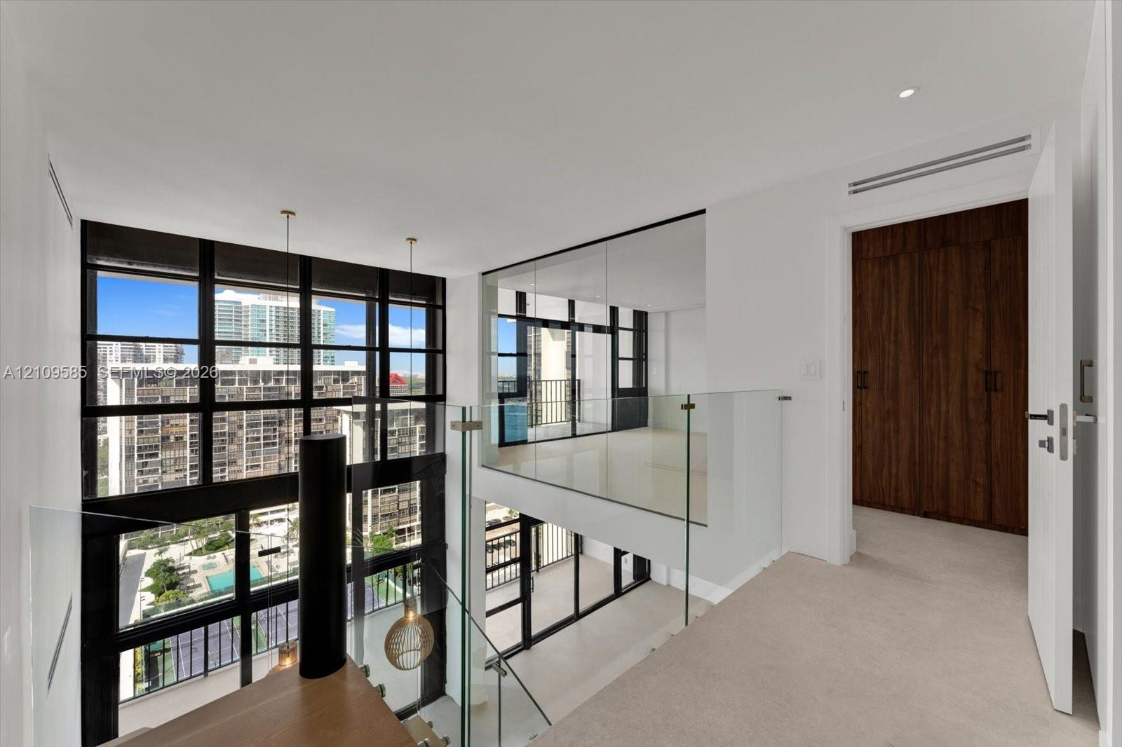 Floor-to-ceiling multi-pane windows, glass-panel railings, wood-finish cabinetry, and neutral carpeting