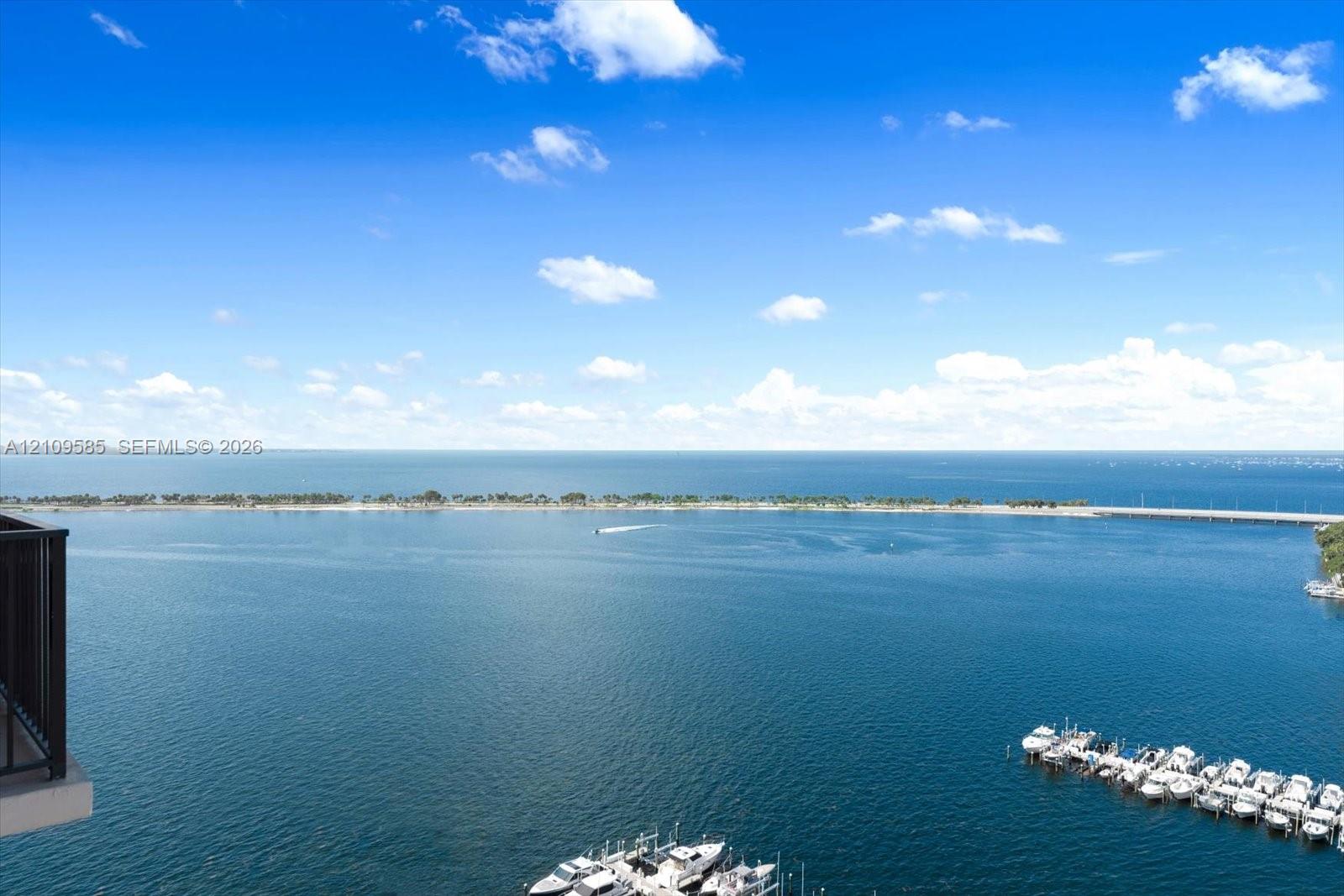 Elevated balcony featuring metal railings with a panoramic water horizon, shoreline, and deep-water marina
